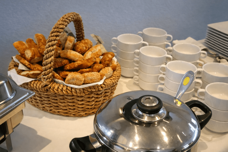Frühstückstisch mit Korb voller frischer Brötchen, weißen Tassen und Kaffeekanne im Gasthaus‑Pension Waldfrieden, Erzgebirge
